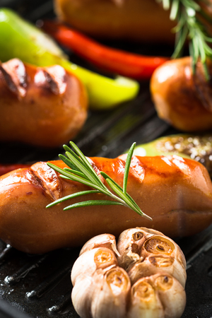 Fried sausages with herbs and vegetables in grill pan at black background.の写真素材