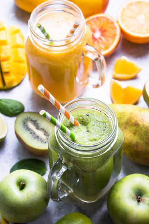 Green and yellow drink. Mango orange juice smoothie and kiwi apple spinach on grey concrete table. Fresh natural drink.の写真素材