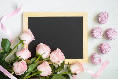 Pink rose and pink dessert around chalkboard at white table. Top view copy space. Mothers day background.の写真素材