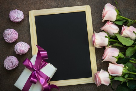 Pink rose present and pink dessert around chalkboard. Top view copy space.  Greeting card background.の写真素材