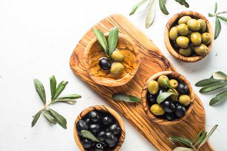 Black and green olives in wooden bowls and olive oil bottle. Top view on white background with space for text.