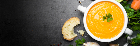 Carrot cream-soup on black table. Vegetarian vegetables soup. Top view. Long banner format.の写真素材
