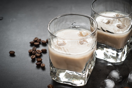 Coffee liqueur in glasses with ice and coffee beans on black table. Close up.