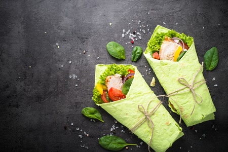 Green spinach tortilla with Chicken and vegetables . Top view with copy space on black slate table. Healthy snack.の写真素材