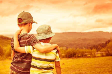 Child in travel trip against the backdrop of forest, meadow, mountains and sky. Rural scene. Two children boys together view from the back. Retro toned.の写真素材