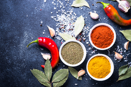 Various spices on dark stone table. Turmeric, paprika, dill, bay leaf, garlic, salt, chili. Top view...