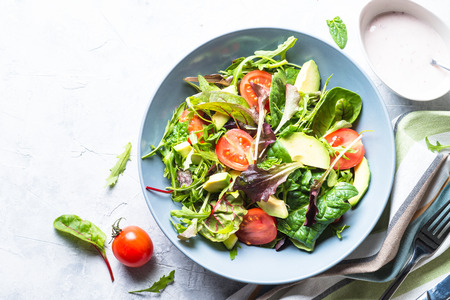 Fresh green salad with mixed green leaves, tomatoes and avocado with yogurt sauce. Clean eating and diet food.の写真素材