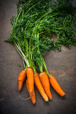 Carrots with green leaves on dark stone table. Top view. Vegetarian food concept.の写真素材