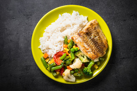 Fish, rise and vegetables in green plate on black background. Healthy food menu. Top view.の写真素材