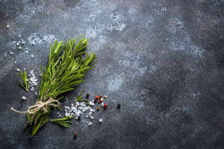 Sprigs of rosemary, pepper and sea salt on a dark stone background. Ingredients for cooking, Top view, Copy space.の写真素材