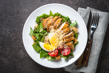 Caesar salad with chicken breast and tomatoes on dark stone table. Top view with copy space.の写真素材