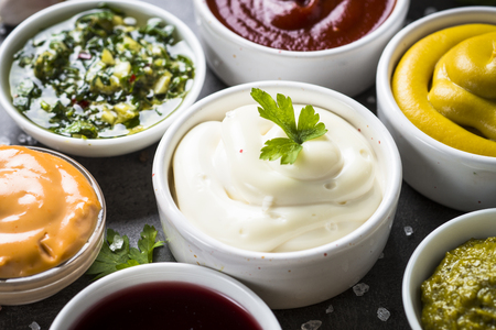 Set of sauces - ketchup, mayonnaise, mustard soy sauce, bbq sauce, pesto, chimichurri, mustard grains and pomegranate sauce on dark stone background.の写真素材