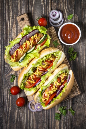 Hot dog with fresh vegetables on dark wooden table.の写真素材