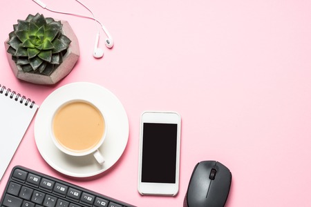 Office workplace with notepad, coffee cup and keyboard on pink background.