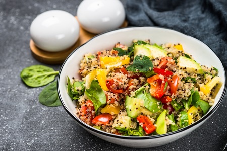 Quinoa salad with spinach, avocado, paprika and tomatoes on black stone table.の写真素材