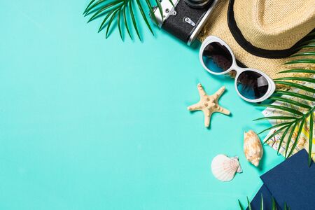 Summer holiday flat lay background. Old film camera, hat, map, sunglasses and palm leaves on blue background. Top view with copy space.の写真素材