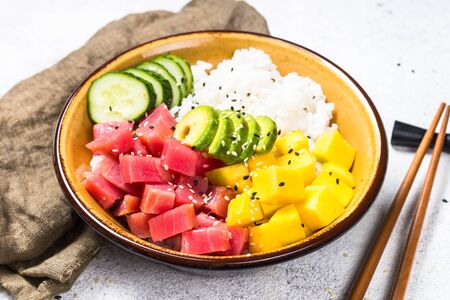 Tuna poke bowl with rice, avocado, mango and cucumber on white table.の写真素材