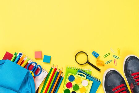 School backpack with stationery on yellow background.