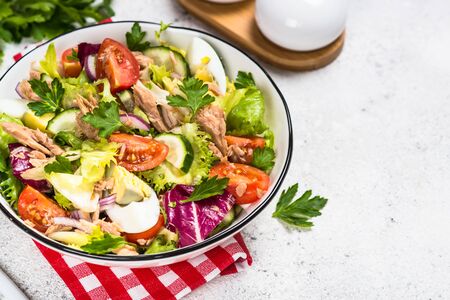 Tuna salad with green leaves, eggs and vegetables in white bowl.の写真素材