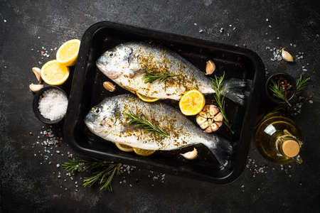 Raw fish dorado in baking sheet at black stone table.