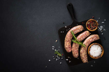 Bratwurst or sausages on cutting board with spices at black table.の写真素材