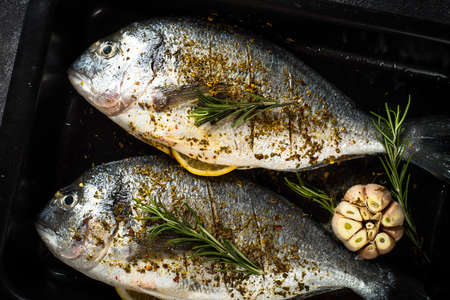Raw fish dorado in baking sheet at black stone table.