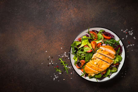 Green salad with baked chicken breast at kitchen table.の写真素材