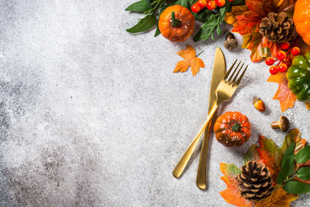 Autumn table setting with white plate, golden cutlery and fall decorations.の写真素材