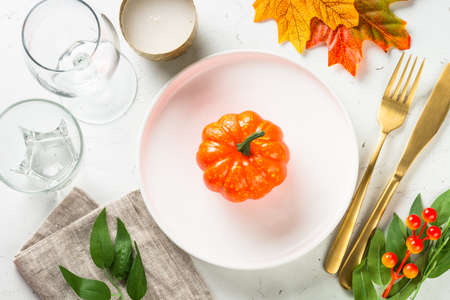 Autumn table setting with white plate, golden cutlery and fall decorations.の写真素材