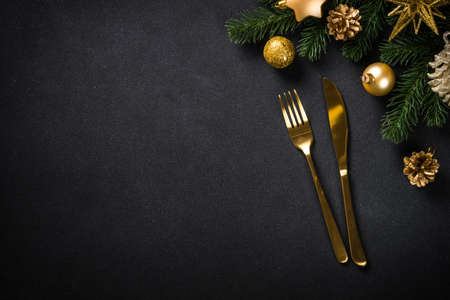 Christmas table setting with golden cutlery and christmas decorations at black background.の写真素材