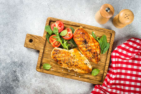 Grilled chicken fillet at wooden cutting board with vegetables.