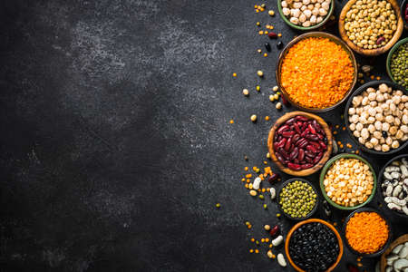 Legumes, lentils, chikpea and beans assortment on black stone table.