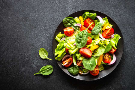 Green salad with fresh vegetables and green leaves at black background.の写真素材