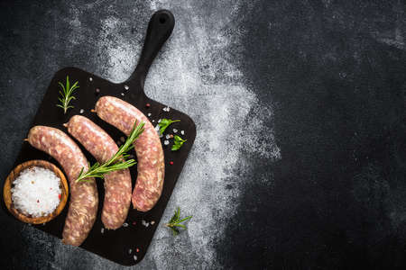 Bratwurst or sausages on cutting board with spices at black table.の写真素材