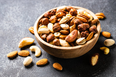 Assortment of nuts in wooden bowl on dark stone table. Cashew, hazelnuts, almonds, brazilian nuts...