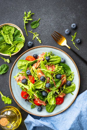 Healthy salad with green leaves, tomatoes and jamon on black.の写真素材
