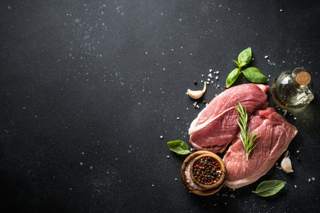 Raw meat steaks with spices, herbs and oil at dark background.の写真素材