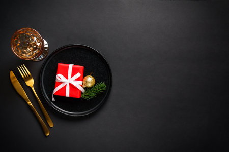 Christmas table setting with black plate, wine glass, cutlery and holidays decorations.の写真素材