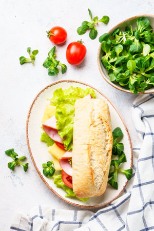 Ciabatta sandwich with lettuce, cheese, tomatoes and ham on white table.の写真素材
