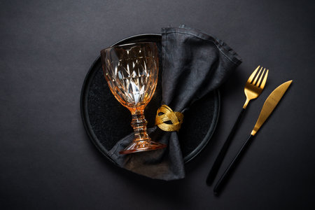 Table setting with black plate, wine glass and golden cutlery.の写真素材