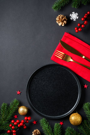 Black Christmas table setting with black plate, wine glass, cutlery and holidays decorations.の写真素材