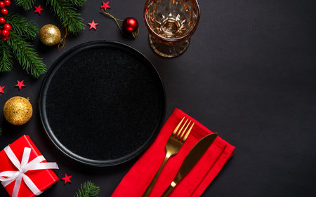 Christmas table setting with black plate, wine glass, cutlery and holidays decorations.の写真素材