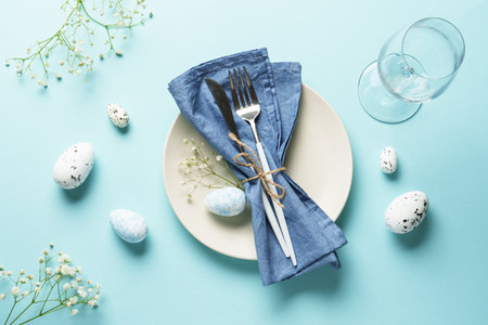 Easter table setting on blue. White plate, cutlery, easter eggs and flowers.の写真素材