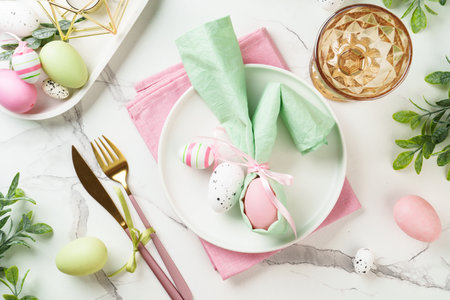 Easter table setting on white background with spring decorations. White plate, cutlery and colored eggs. Flat lay.の写真素材