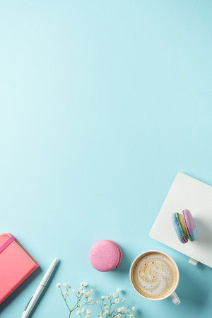 Office workspace flat lay. Cup of coffee, macaroon and flower on blue background.の写真素材