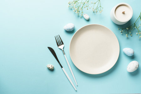 Spring table setting on blue. Empty plate, cutlery, easter eggs and flowers. Flat lay image with copy space.の写真素材