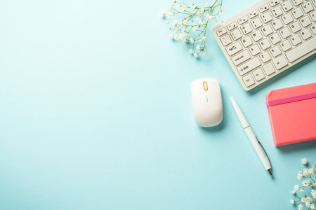 Office desk with keyboard, notebook, pen and flowers on blue background. Flat lay with copy space.の写真素材