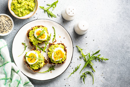 Avocado sandwich. Whole grain bread with avocado and boiled eggs with arugula. Top view on white background.の写真素材