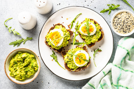 Open sandwich. Whole grain bread with avocado and boiled eggs. Top view on white kitchen table.の写真素材