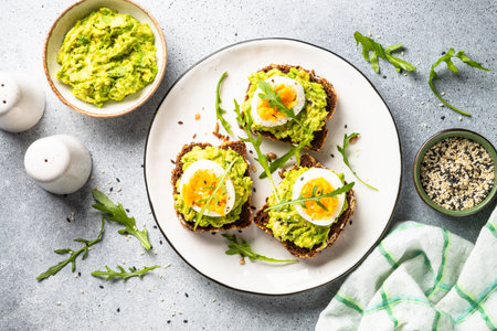 Open sandwich. Whole grain bread with avocado and boiled eggs. Top view on white kitchen table.の写真素材